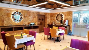 A restaurant with a modern interior, featuring a central dining area with tables and chairs, a bar area with a counter and stools, and decorative wall mirrors. - My Garden Hotel (Istanbul)