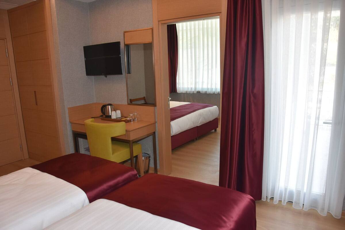 A hotel room with two beds, a desk with a chair, a television, and a window with curtains.