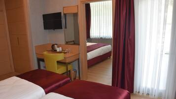 Quarto de hotel com duas camas, uma mesa de trabalho com cadeira, televisão e janela com cortinas.