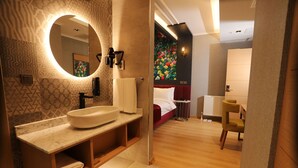A modern bathroom with a large oval sink, a mirror, and a toilet. There is a small round table with a chair, a radiator, and a wall with a floral mural. - My Garden Hotel (Istanbul)