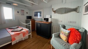 A cozy room with a bed, a desk with a computer, a chair, and a microwave on a cabinet.