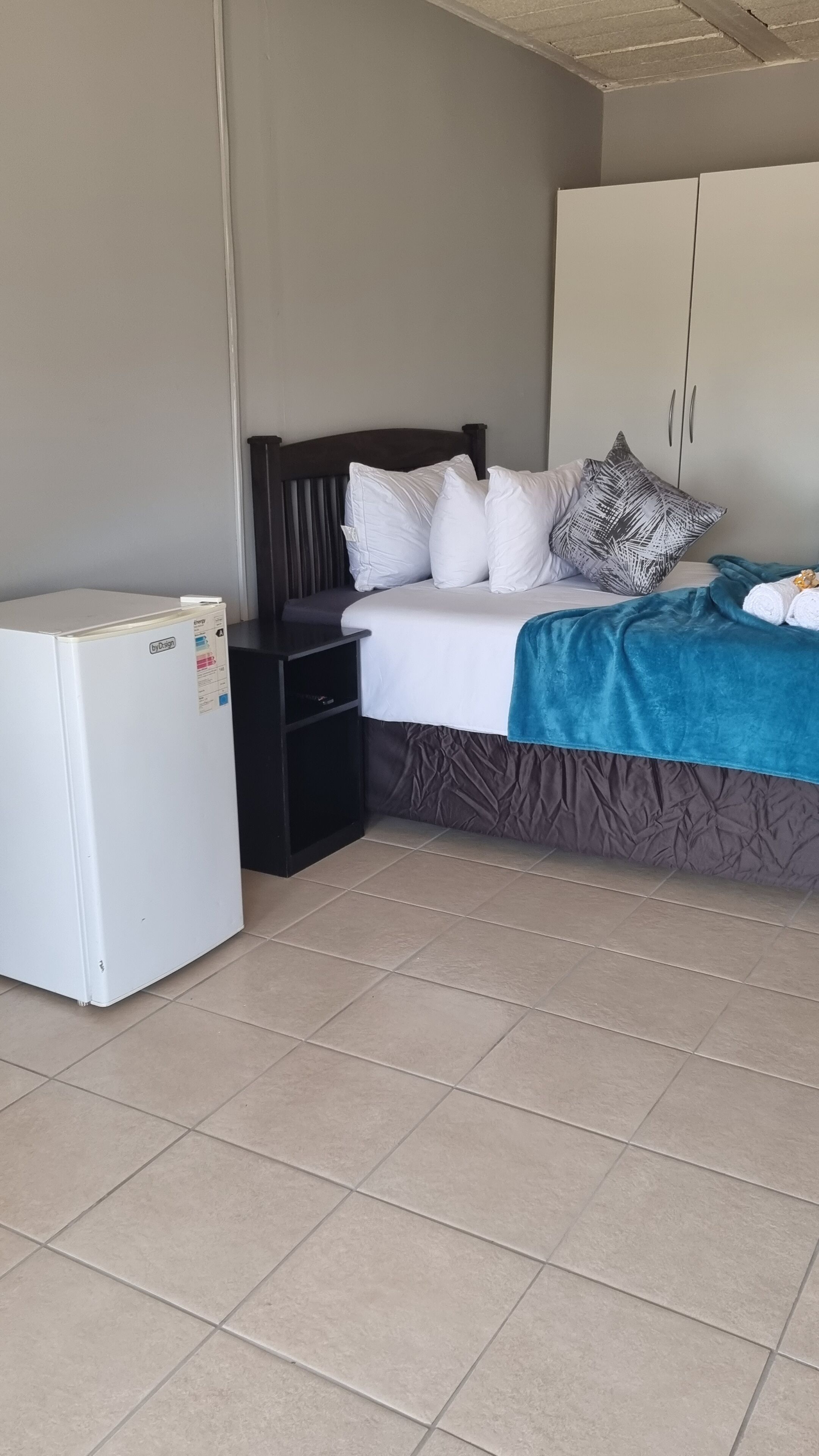 A bedroom with a bed, a nightstand, a wardrobe, and a white refrigerator.