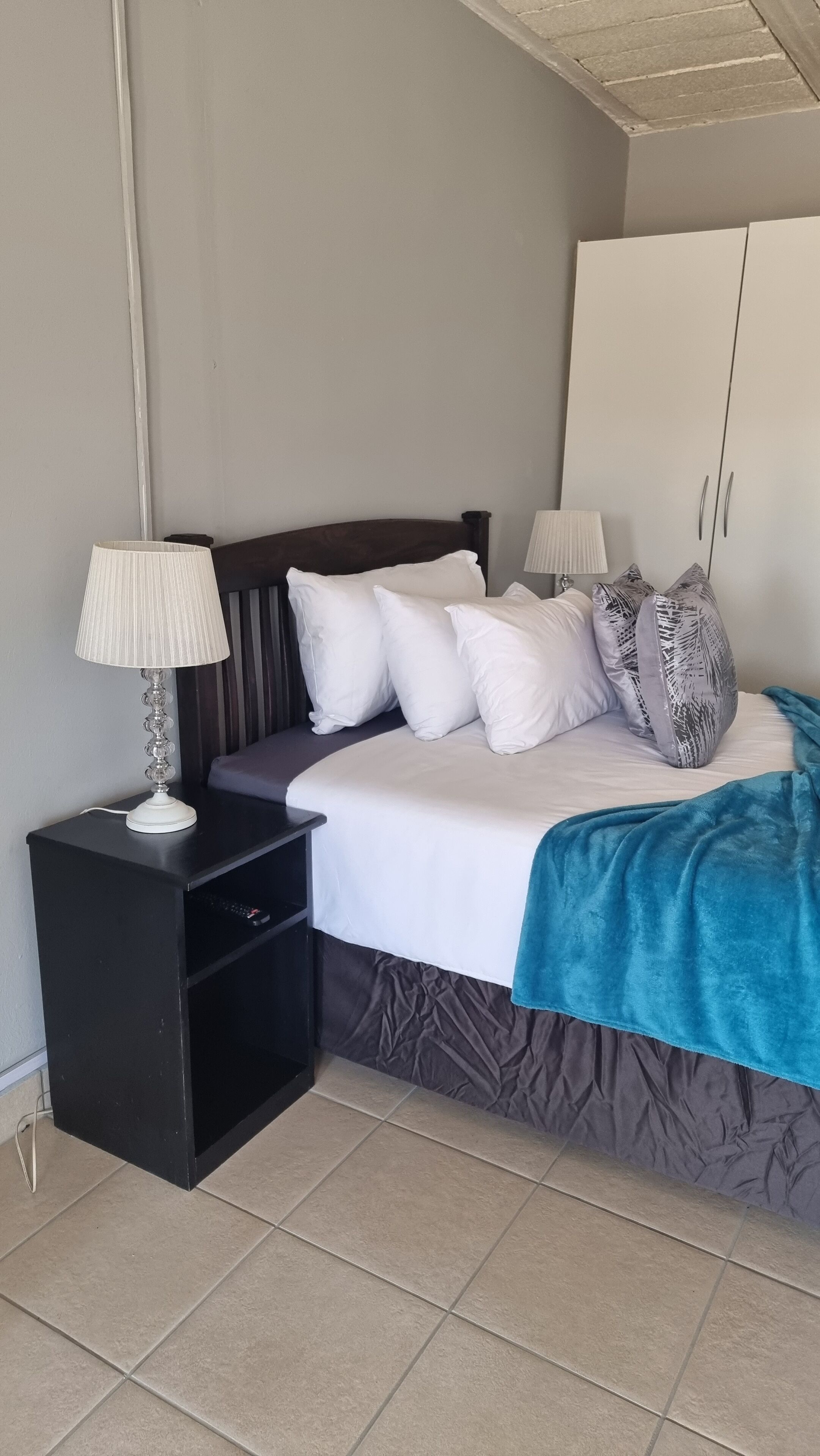 A bedroom with a bed, two bedside tables, a nightstand, a wardrobe, and a ceiling light fixture.