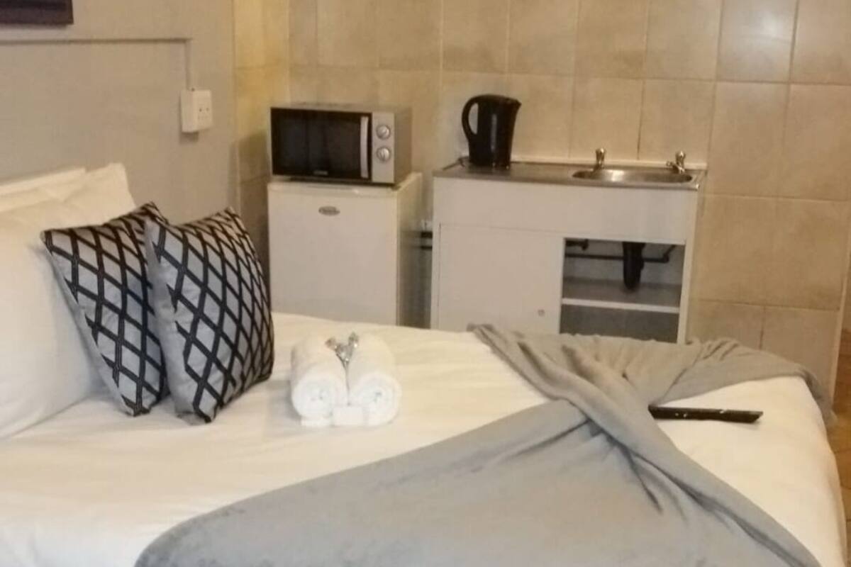 Una habitación de hotel con una cama, una mesita de noche con hervidor, microondas y un lavamanos pequeño.