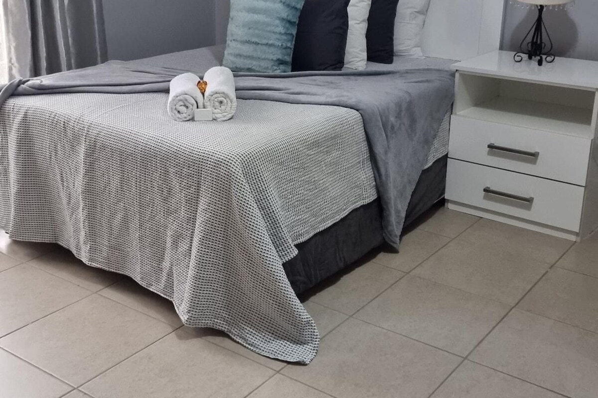 Um quarto bem arrumado com cama, almofadas, mesa de cabeceira e abajur.