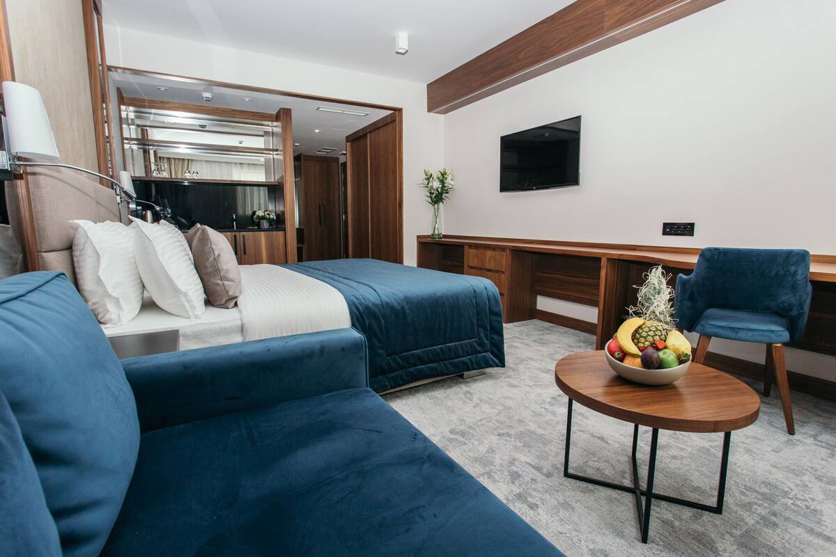 A modern hotel room with a bed, a desk, a chair, and a small table with fruit.
