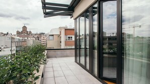 A modern balcony with large glass doors, a tiled floor, and a view of surrounding buildings and a church. - Central Point Hotel (Belgrade)