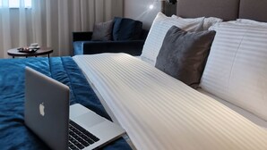 A hotel room with a large bed, a laptop on the bed, a small table with a tray of food, and a window with curtains. - Central Point Hotel (Belgrade)
