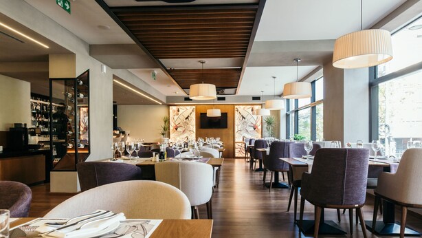 A modern restaurant with wooden flooring, high tables, and comfortable chairs. - Central Point Hotel (Belgrade)