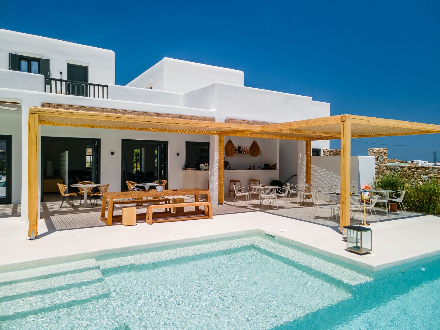 A modern white building with a pool, outdoor seating, and a view of the sea.