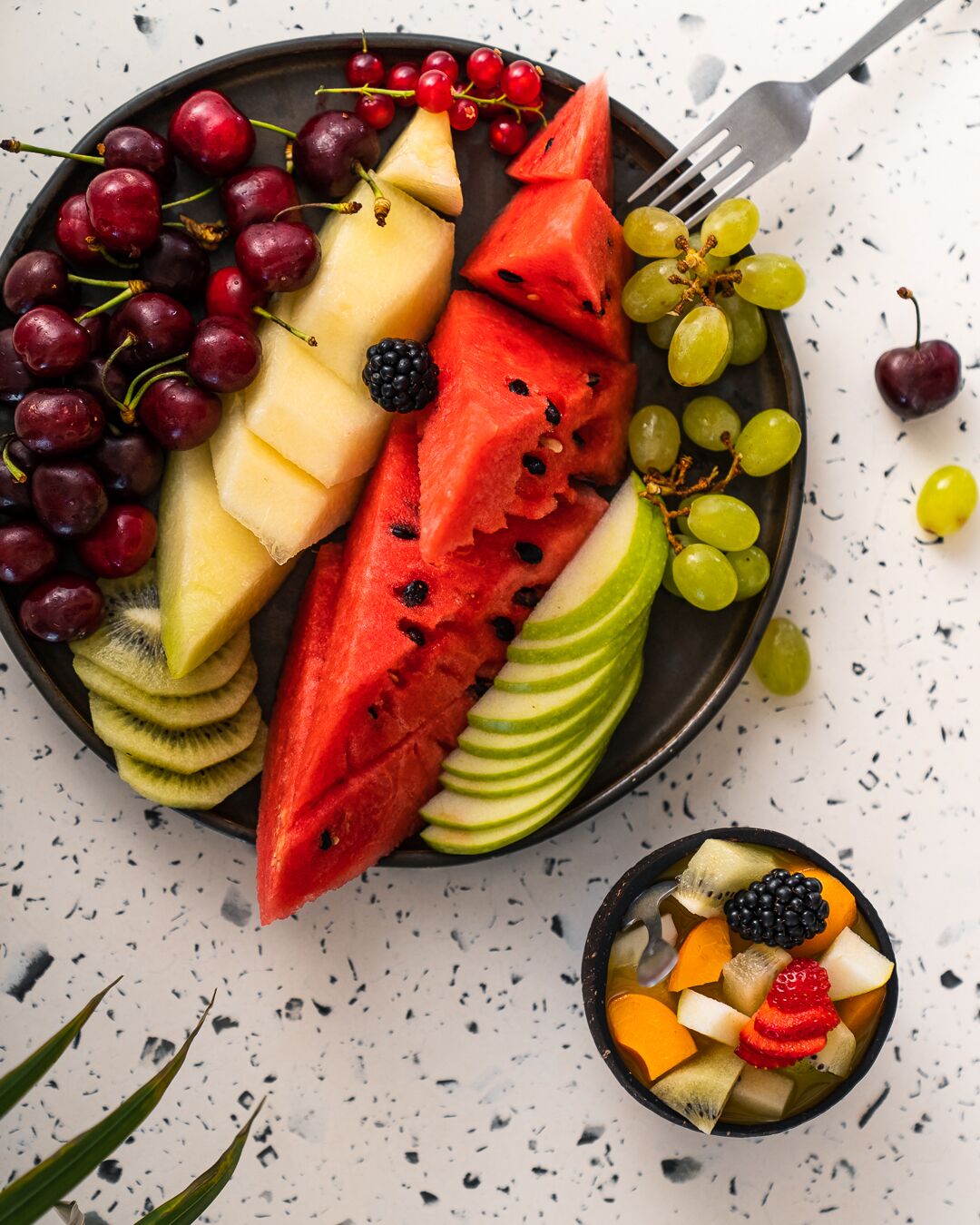Une assiette de fruits comprenant de la pastèque, des raisins, des kiwis et d’autres fruits.