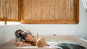 A person relaxing in a bathtub with a flower vase and a drink. - Koukoumi Vegan Boutique Hotel (Mykonos)