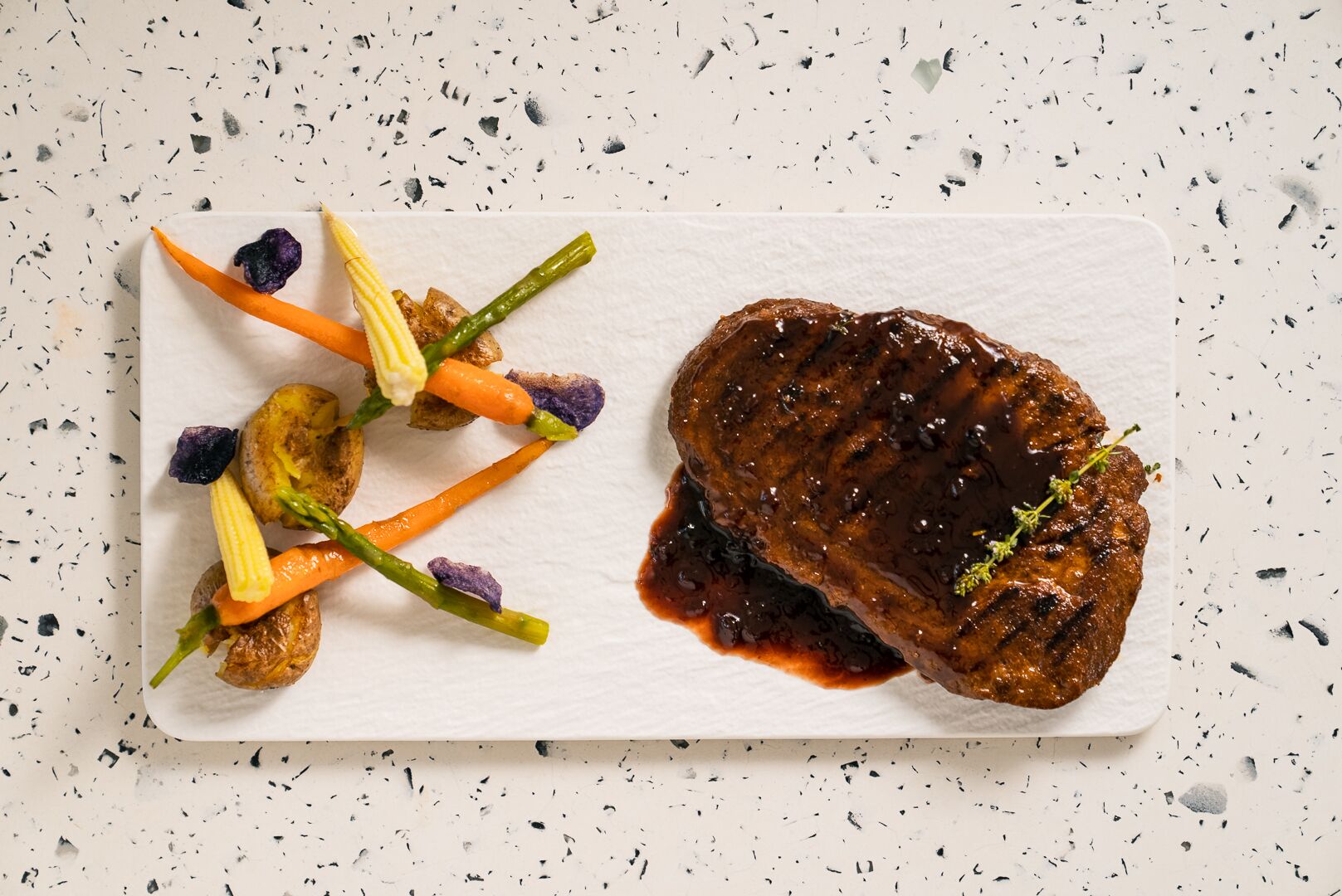 Ein angerichtetes Gericht mit einem Steak und Gemüse auf einem weißen Teller.