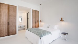 A bedroom with a large bed, a bedside table, a hanging light, and a wardrobe. - Koukoumi Vegan Boutique Hotel (Mykonos)