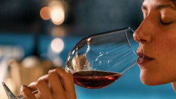 Una persona sosteniendo una copa de vino con un líquido oscuro, probablemente vino, en un ambiente tenuemente iluminado, con una piscina al fondo.
