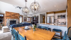 A modern kitchen with stainless steel appliances, a dining area with a wooden table and blue chairs, and a stone fireplace. - Les Falaises by Tremblant Platinum (Mont-Tremblant)