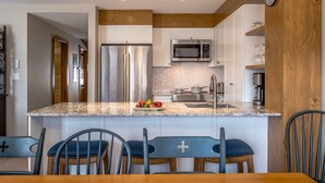 A modern kitchen with a central island, stainless steel appliances, and a wooden accent wall. - Les Falaises by Tremblant Platinum (Mont-Tremblant)