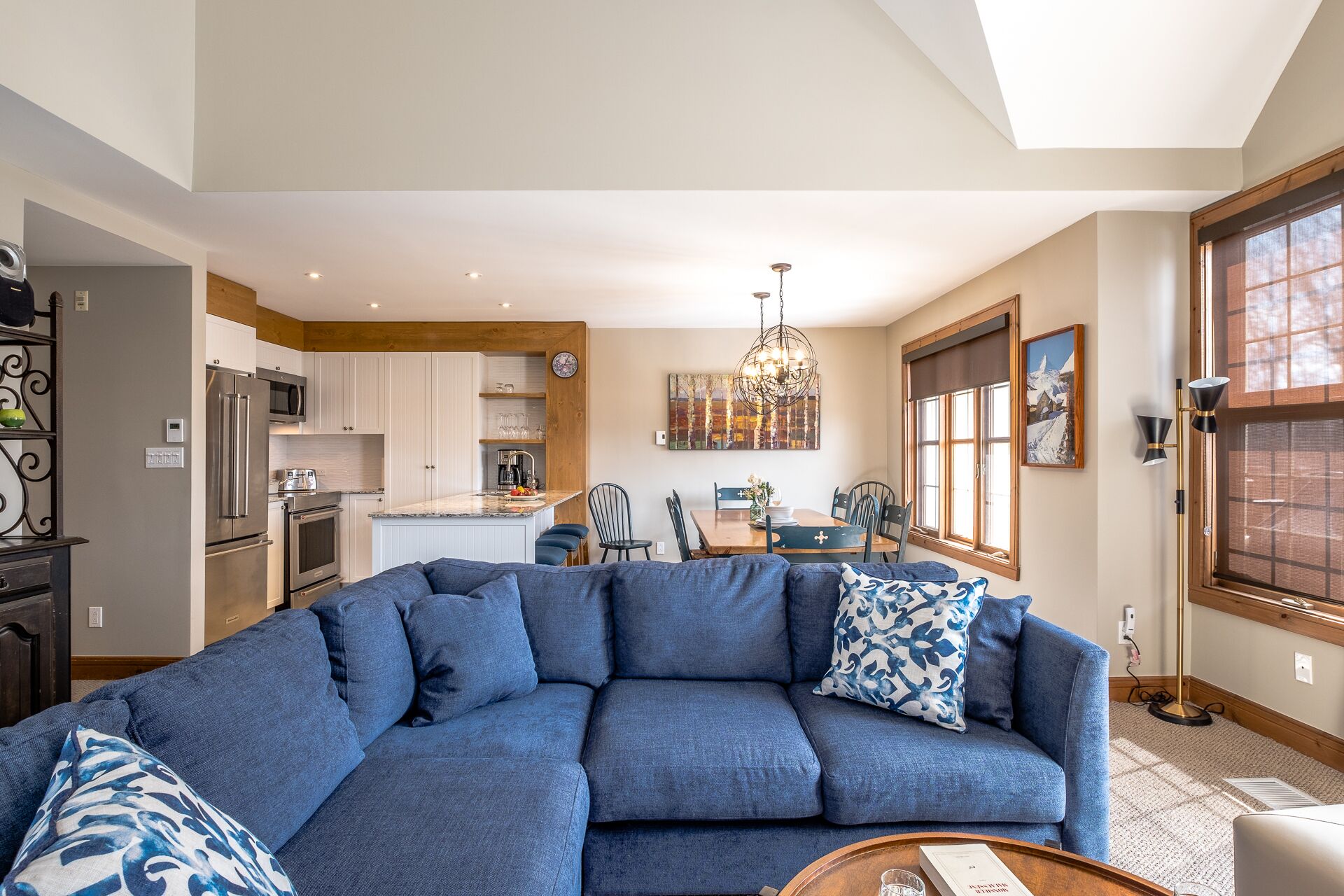A modern living room with a sectional sofa, a dining area with a wooden table, and a kitchen with stainless steel appliances.