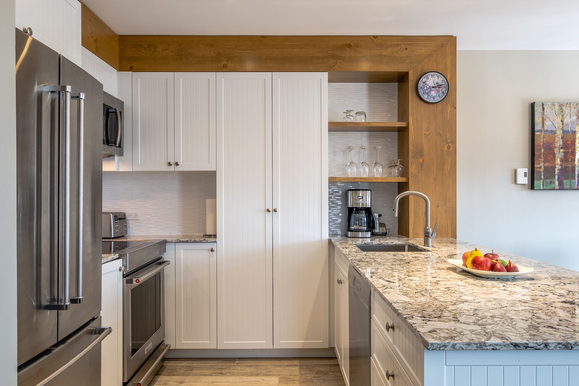 A compact kitchen with white cabinetry, a stainless steel refrigerator, a built-in oven, a coffee maker, and a sink with a wooden countertop.
