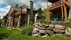 A large, multi-story lodge with a stone chimney, wooden balconies, and a stone retaining wall. - Les Falaises by Tremblant Platinum (Mont-Tremblant)