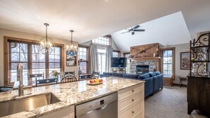 A spacious kitchen with a large island, a dining area with a chandelier, and a living room with a blue sofa. - Les Falaises by Tremblant Platinum (Mont-Tremblant)