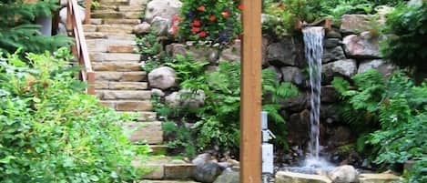 Eine Steintreppe führt zu einem Wasserfall in einer üppigen Gartenanlage.