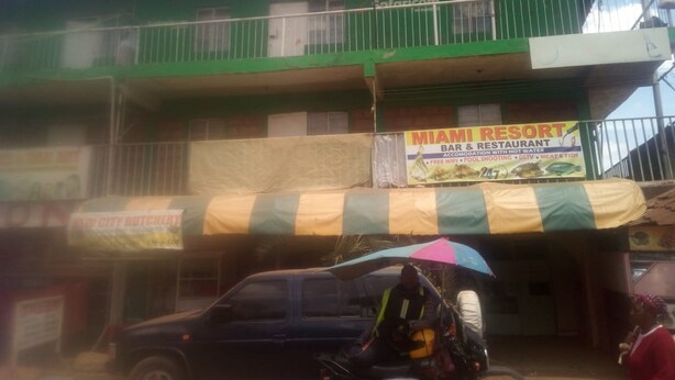 A building with a green facade, a sign for 'MIAMI RESORT BAR & RESTAURANT' advertising hot water, free WiFi, pool shooting, DSV, meat & fish, and a phone number.
