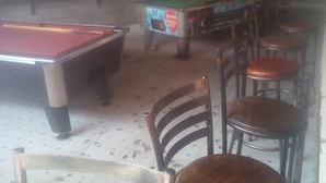 A billiards table, a pool table, and several wooden chairs in a room with tiled flooring.