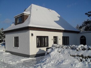 A snow-covered single-story house with a gabled roof and a chimney.