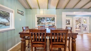 Comedor con mesa y sillas de madera, ventanas amplias con vistas y techo con vigas a la vista.