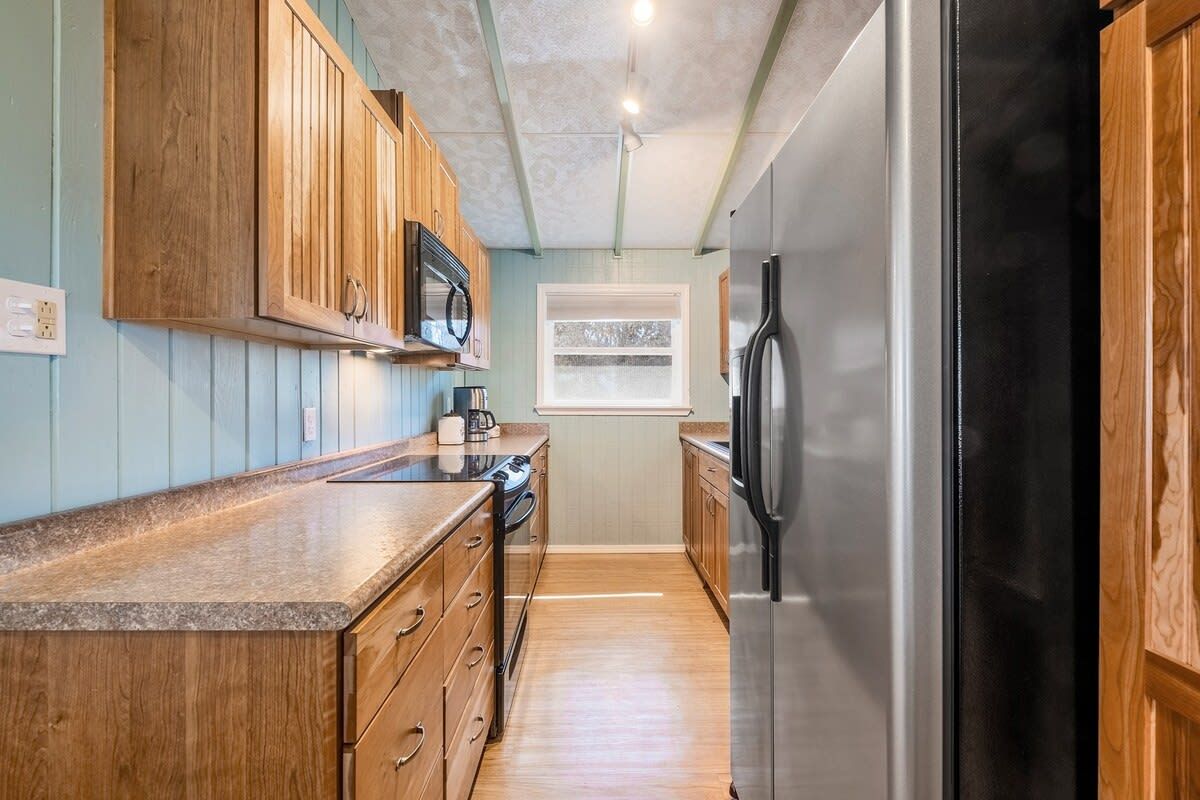 A kitchen with wooden cabinets, a stainless steel refrigerator, and a window with a view.