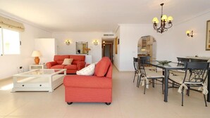 A spacious living room with a red sofa, a glass coffee table, and a dining area with a glass table and chairs.