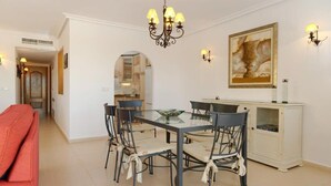 A dining area with a glass-top table, six chairs, a chandelier, wall sconces, and a cabinet with glass doors.