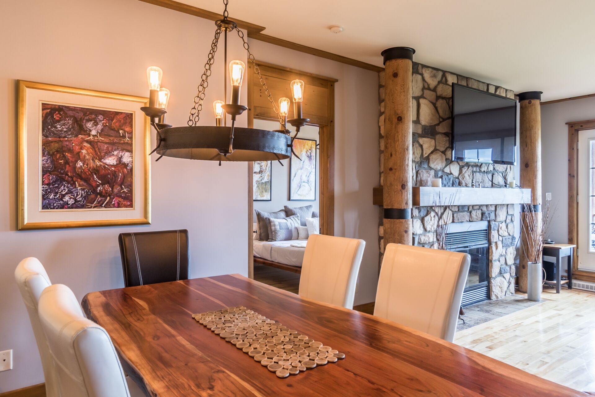 A dining area with a wooden table, chairs, a chandelier, and a stone fireplace.