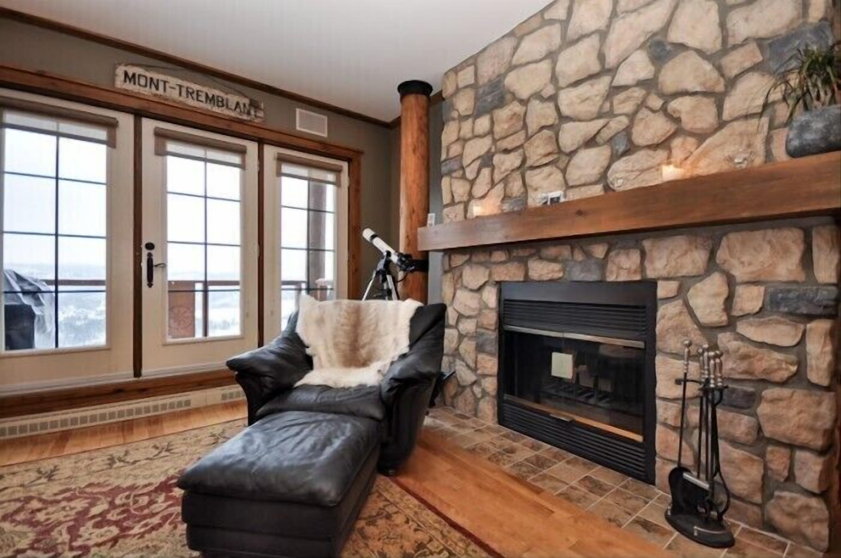 A cozy living room with a stone fireplace, leather sofa, and a sign reading "MONT-TREMBLANT".