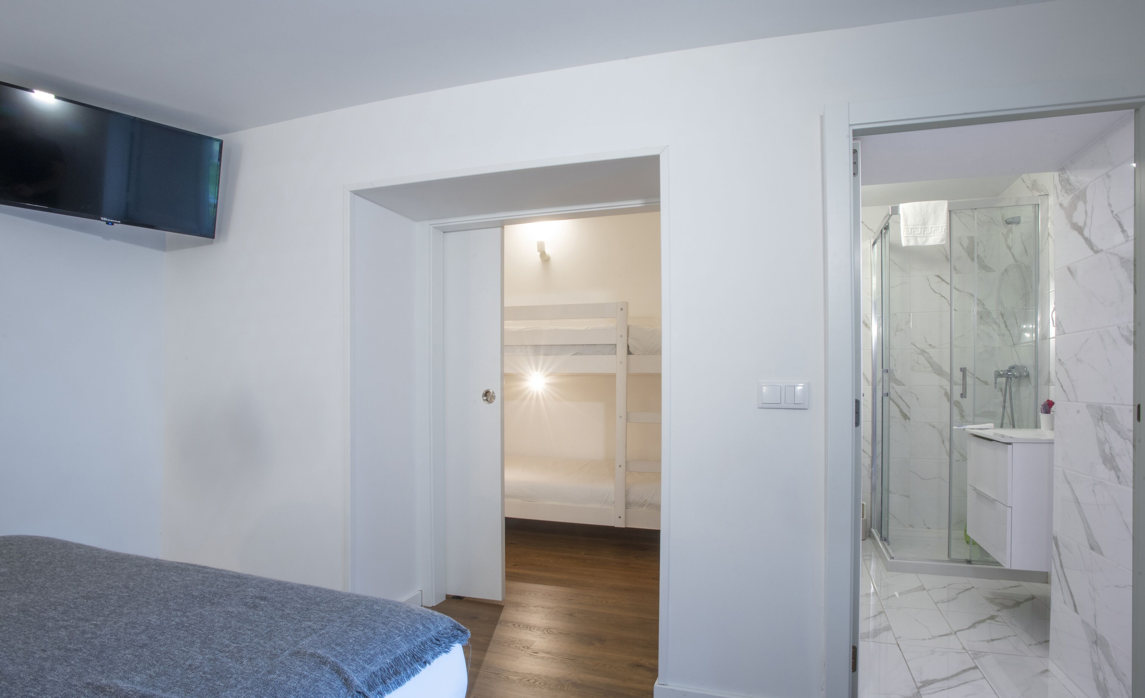 Une chambre moderne avec un lit, un téléviseur fixé au mur et une salle de bain dotée d’une douche à parois de verre.
