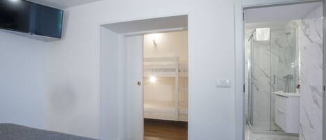 Une chambre moderne avec un lit, un téléviseur fixé au mur et une salle de bain dotée d’une douche à parois de verre.