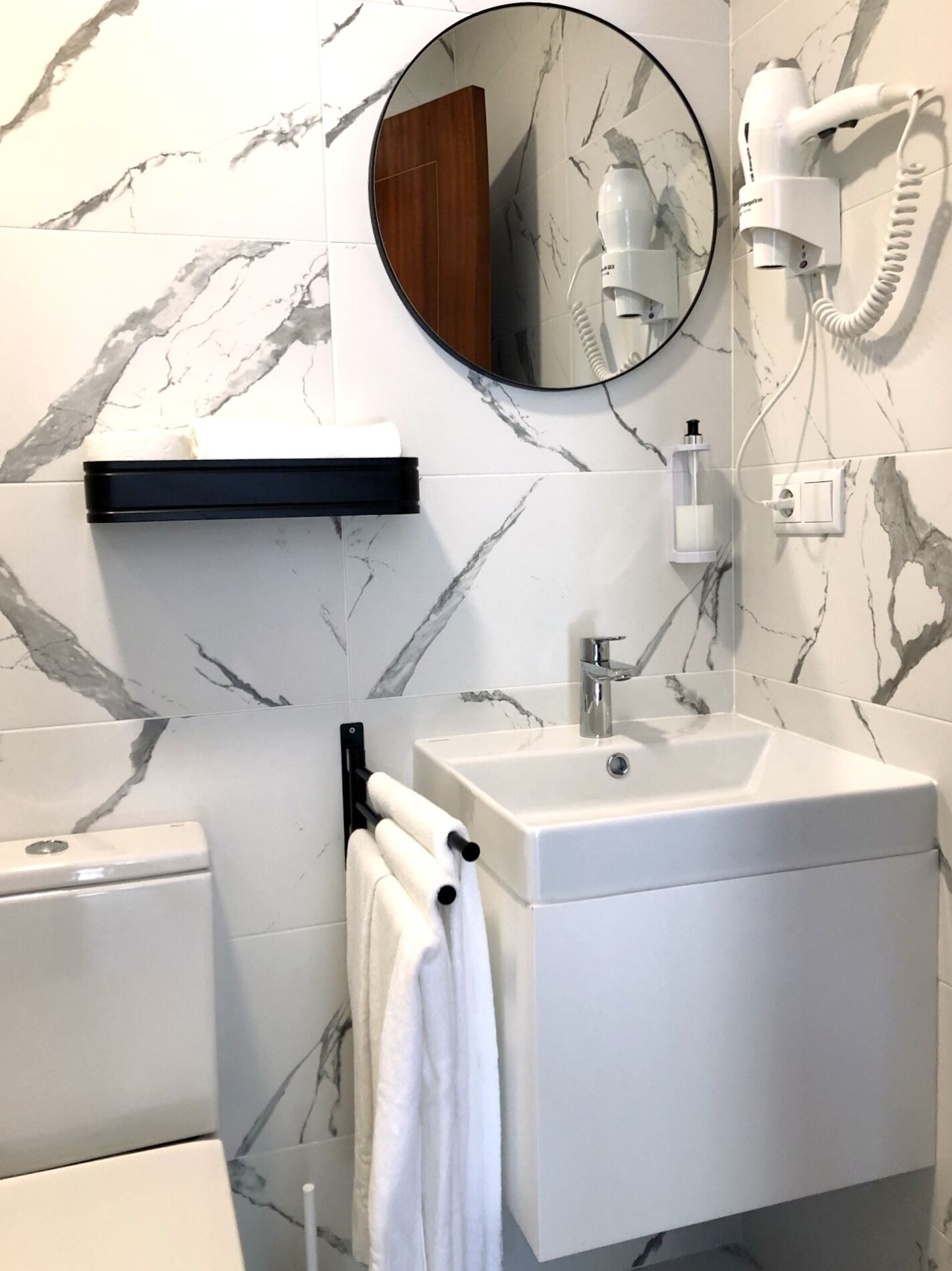 A bathroom with a white sink, a mirror, a towel rack, and a hairdryer mounted on the wall.