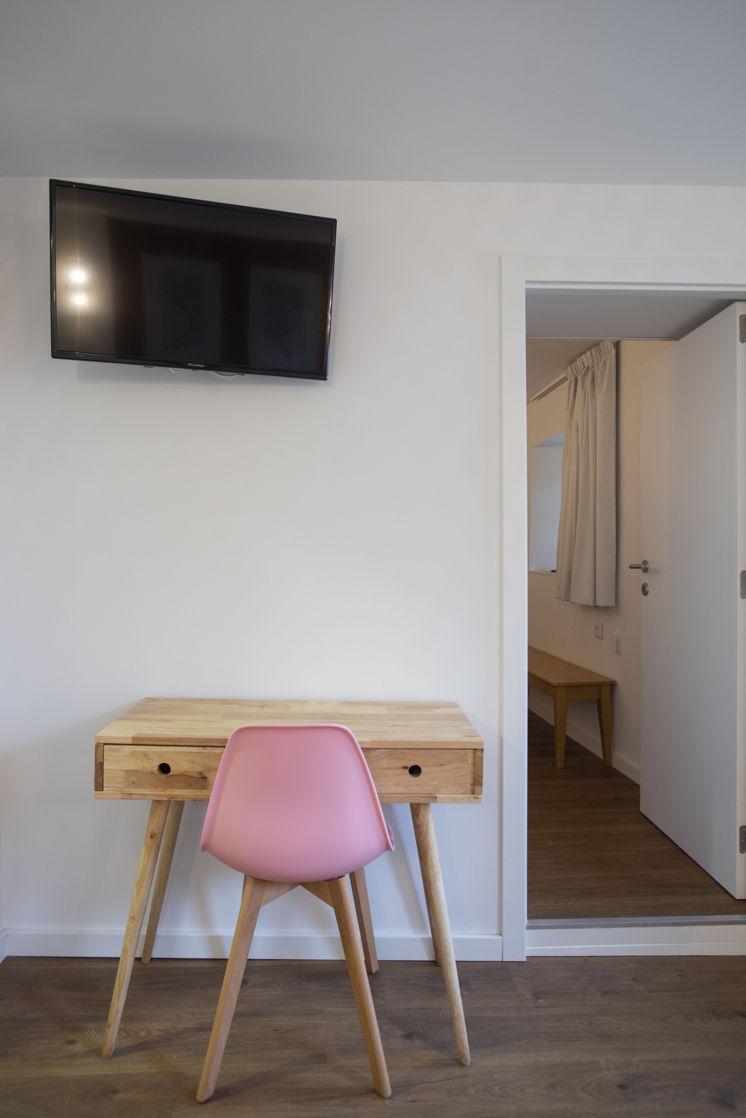 Une pièce avec un bureau en bois, une chaise rose et un téléviseur à écran plat fixé au mur.