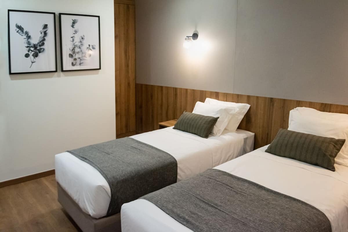 Hotellihuone, jossa on kaksi sänkyä, puinen pääty, yöpöytä ja kaksi kehystettyä kasvitaiuluista seinällä.