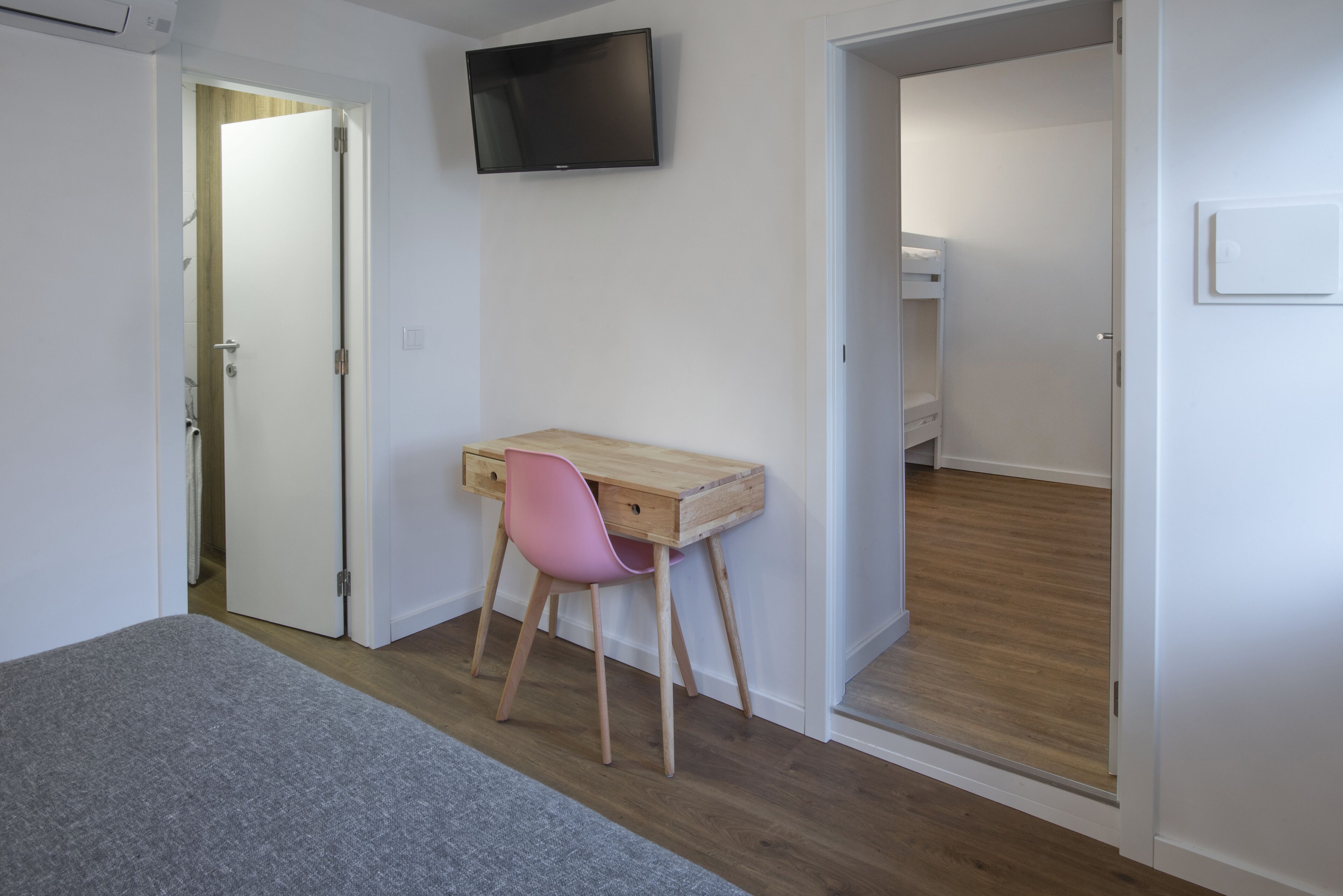 Une chambre à coucher avec un lit, un bureau et une chaise, un téléviseur fixé au mur et une porte de salle de bain.