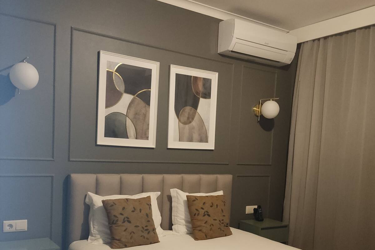 Hotellihuone, jossa on sänky, kaksi seinälle asennettua valaisinta ja kaksi kehystettyä abstraktia maalausta.