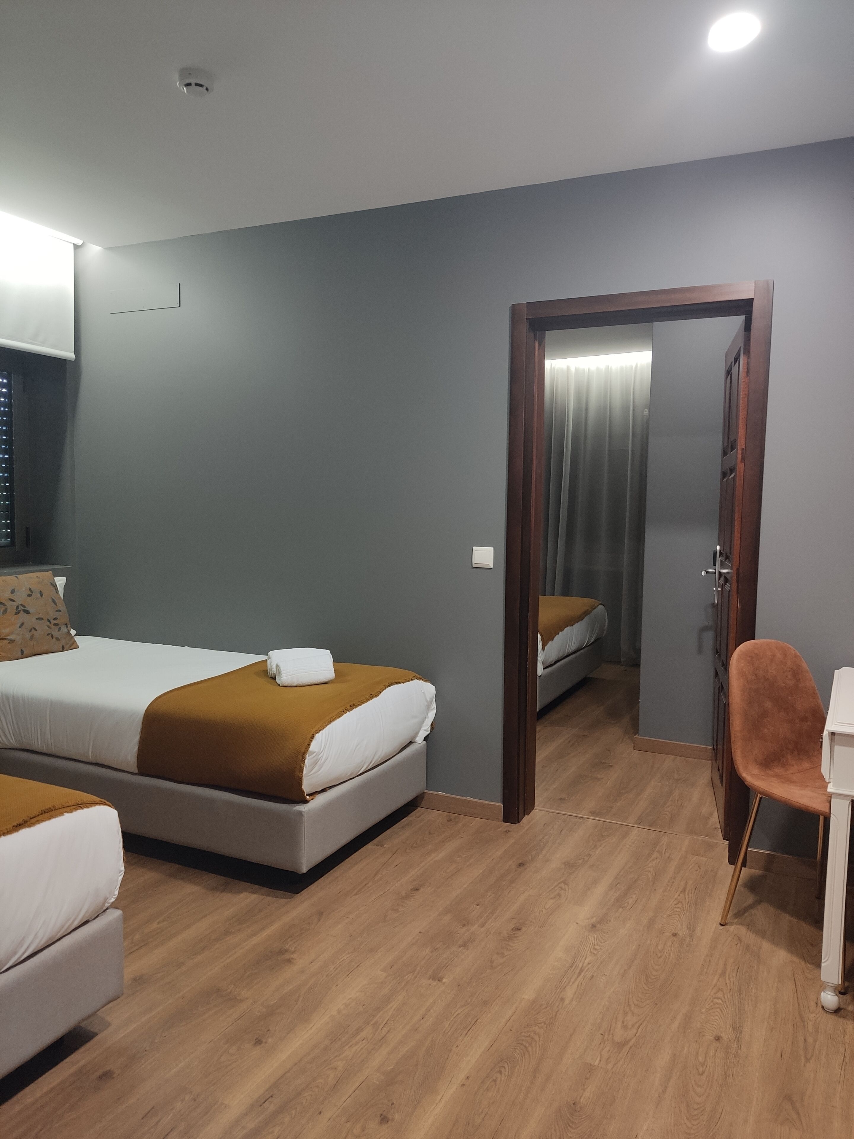 A hotel room with two beds, a wooden floor, a mirror, and a chair.