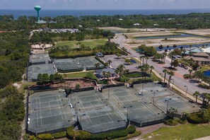 An aerial view of a large sports complex with multiple tennis courts, a water tower, and surrounding greenery.
