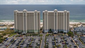 Ein Hochhaus-Hotel mit mehreren Etagen, einem Parkplatz und einem Strand im Hintergrund.