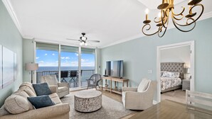 Ein geräumiges Wohnzimmer mit Balkon, Essbereich und Schlafzimmer mit großem Bett und Fernseher.