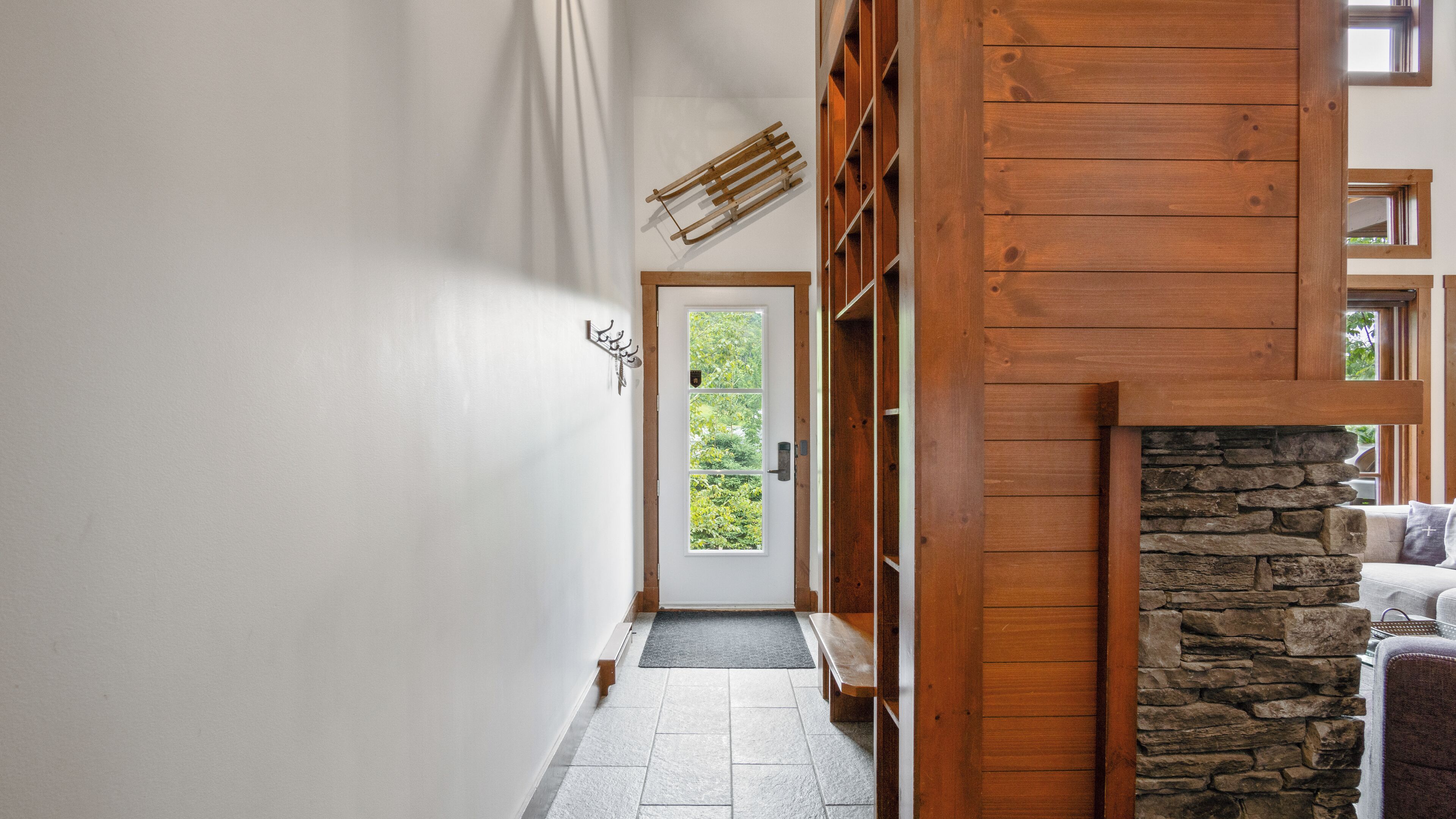 A hallway with a wooden door, a stone fireplace, and a view of greenery outside.