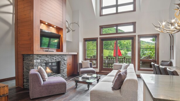 A spacious living room with a stone fireplace, comfortable seating, and large windows offering a view of the outdoors.