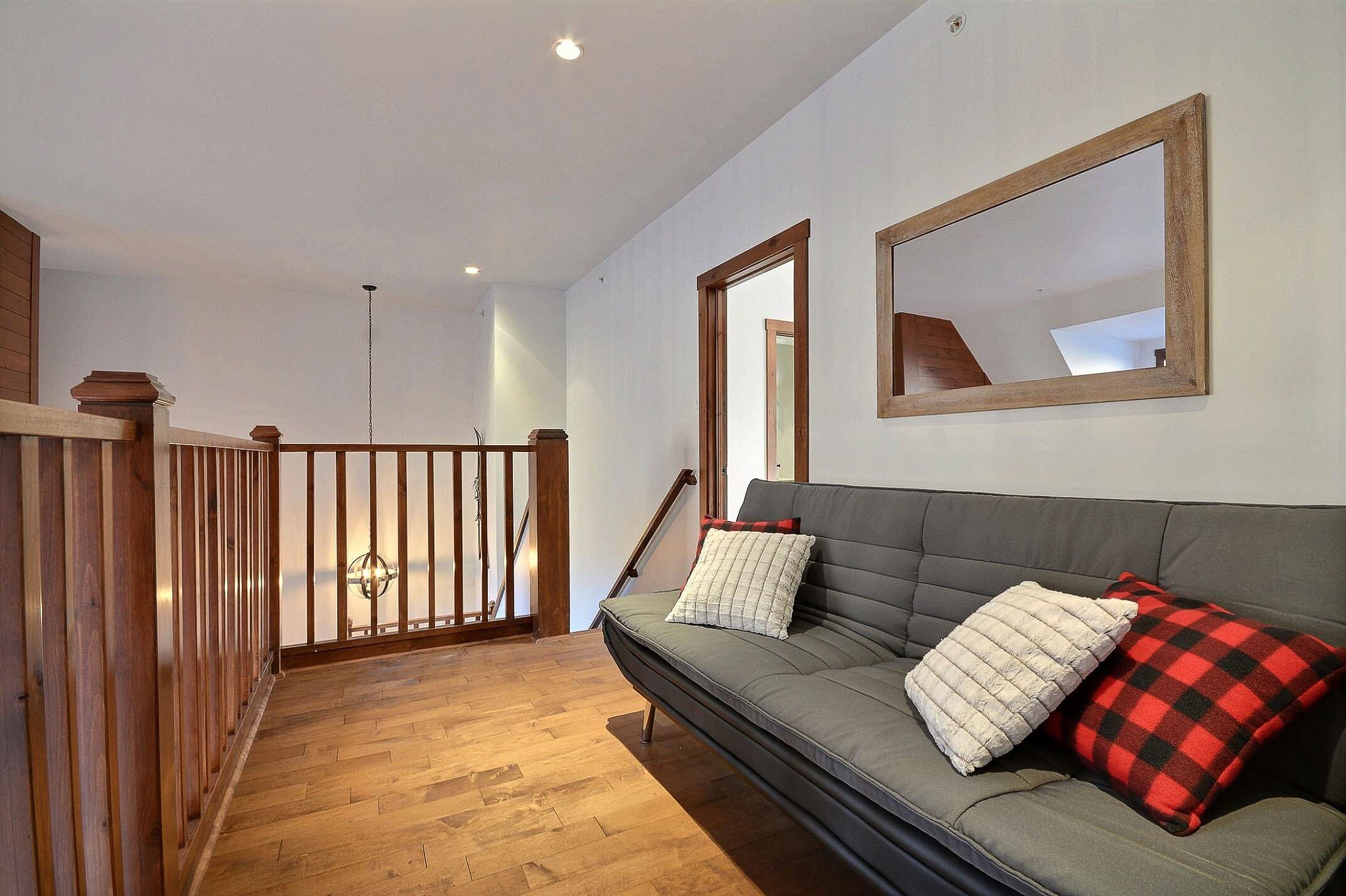 A modern interior with a grey sofa, wooden floor, and a wooden railing.