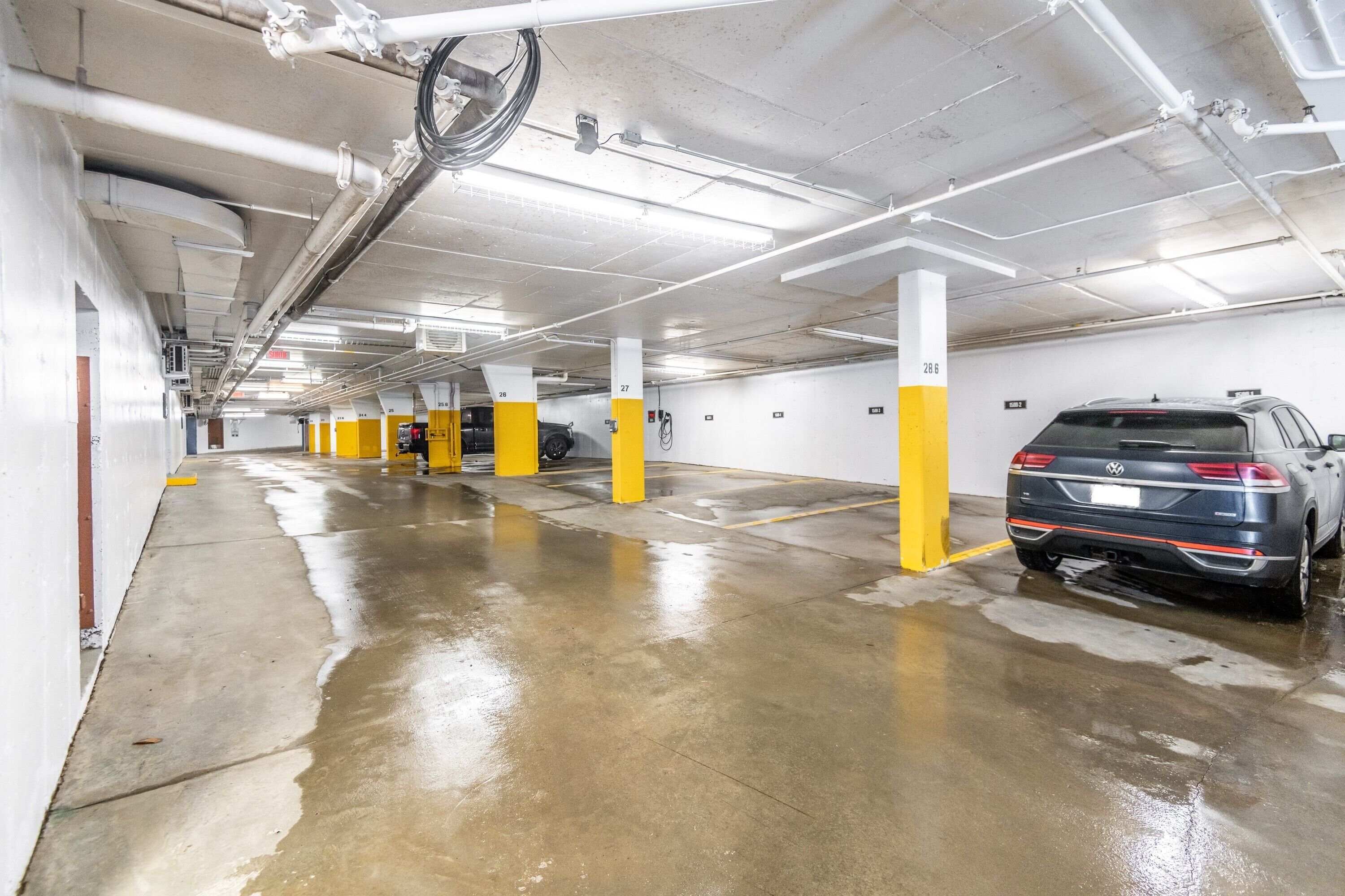 A multi-level parking garage with wet floors, yellow pillars, and a parked car.